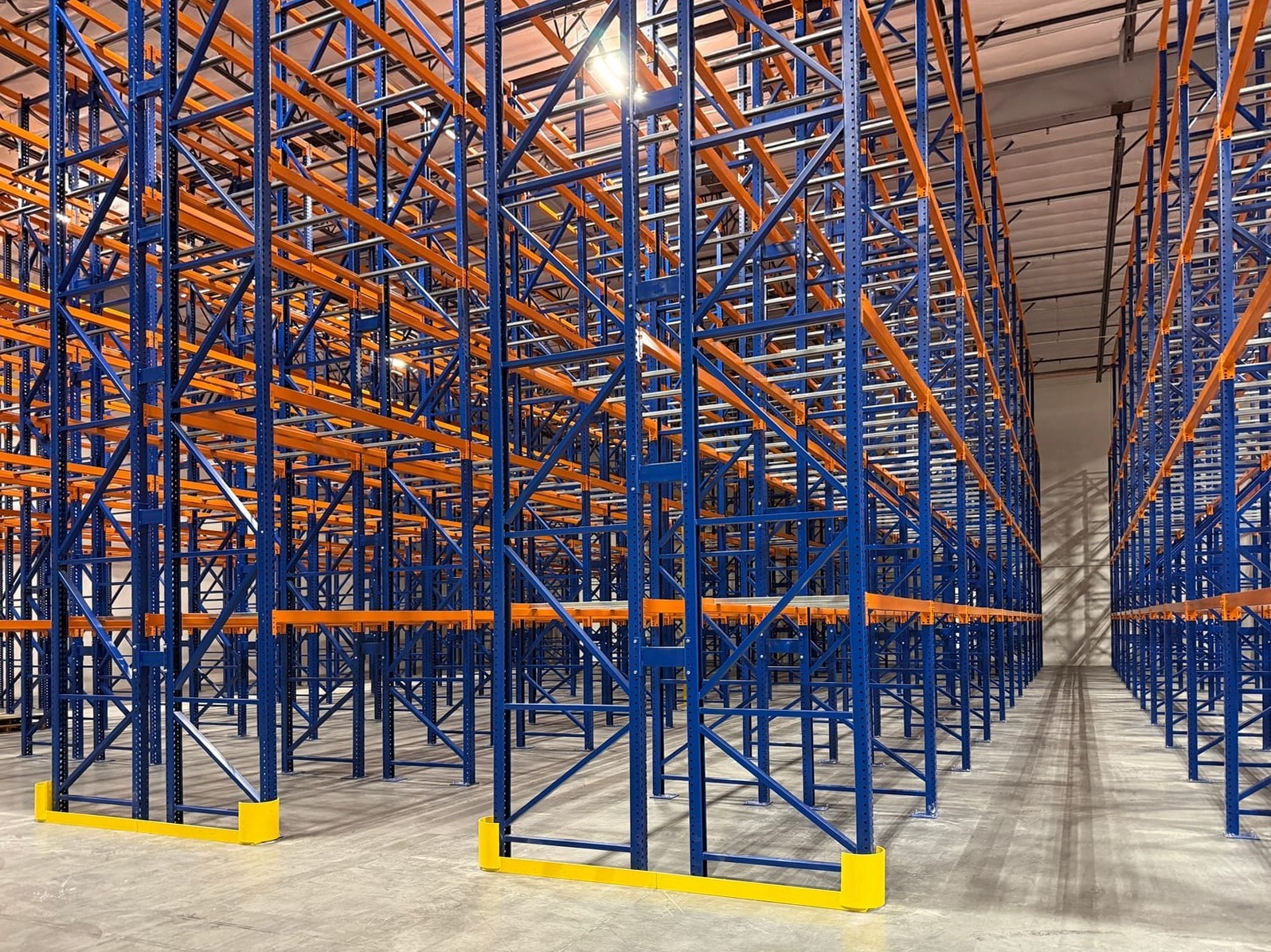 Rows of tall blue and orange selective pallet racking with yellow end-of-aisle guards in a temperature-controlled warehouse installed by Hammerhead