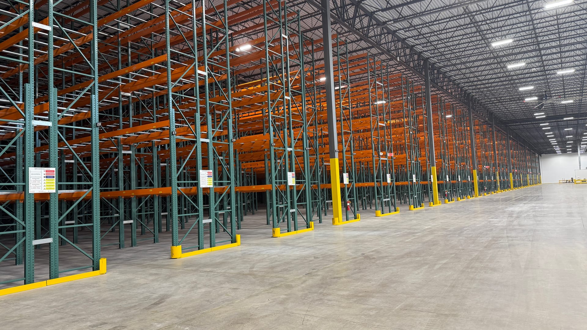 Long run of selective pallet racking receding down a distribution center aisle, with load placards and column protection at every upright