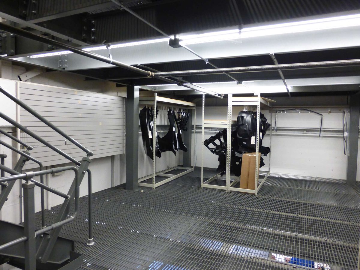 Open bar grating decking on a parts storage mezzanine, with light from the floor below showing through the deck
